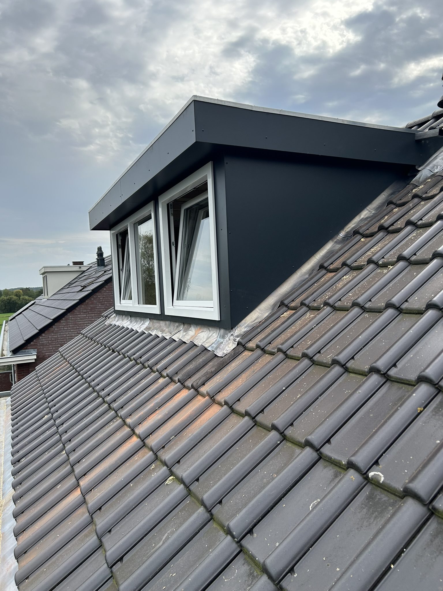 Zijaanzicht van een antraciet Trespa dakkapel met witte kozijnen en weggewerkte rolluiken door C.H. Montage.